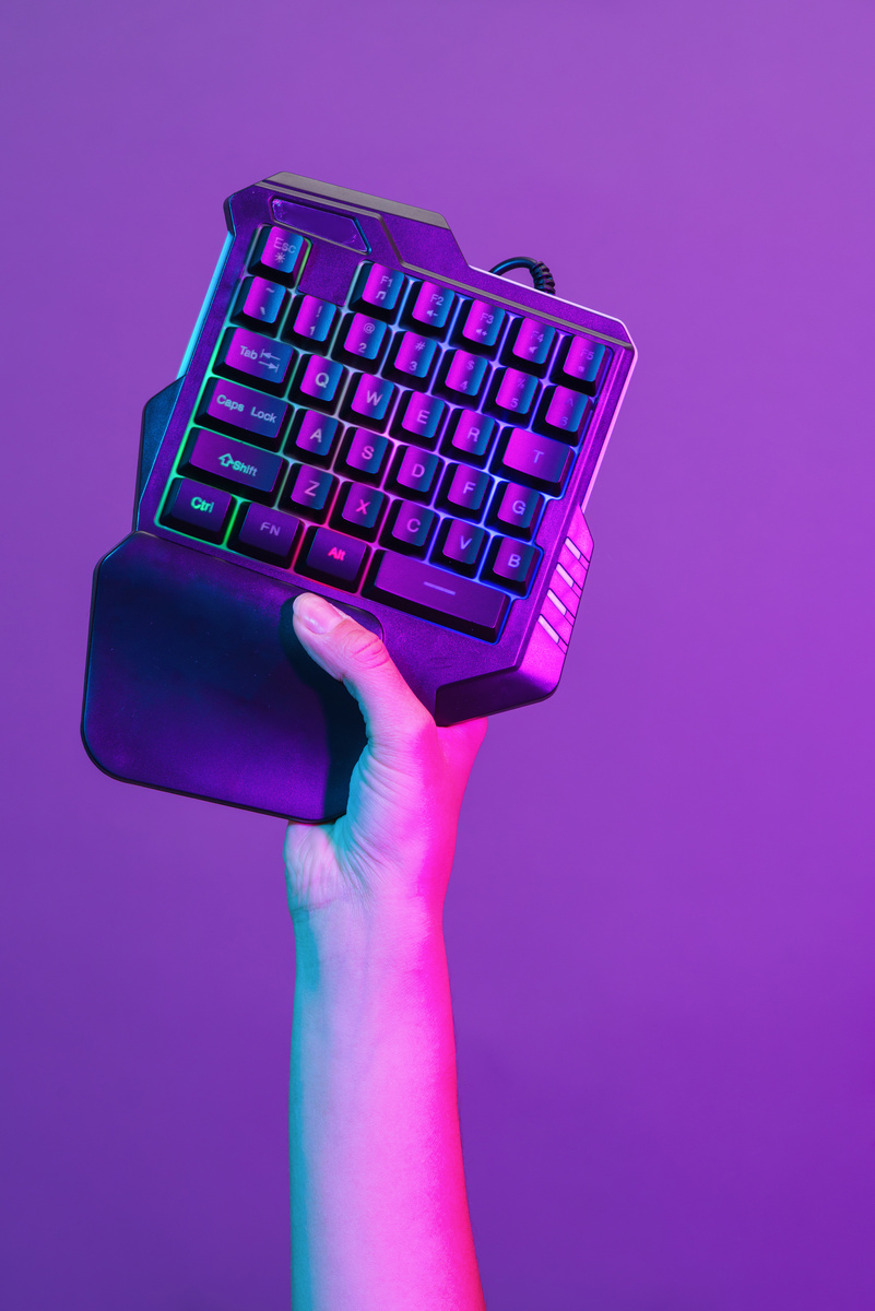 Hand with gamers keyboard on violet background.